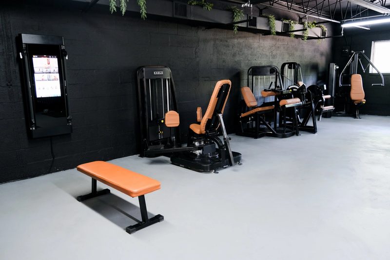 A row of selectorized cardio and strength machines along a black wall