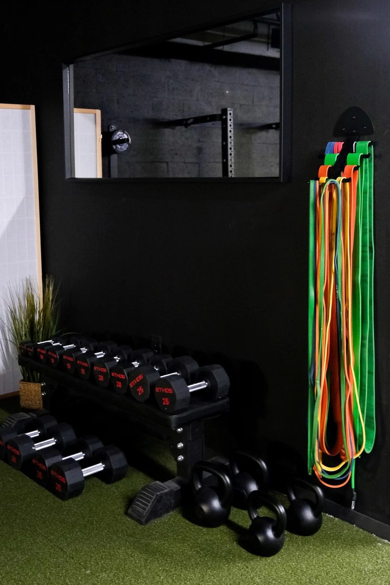 A dumbbell rack, kettlebells and resistance bands beside a mirror